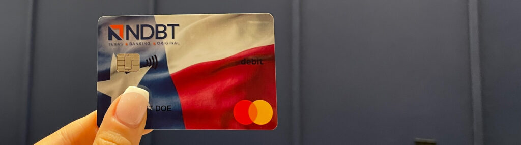 Closeup of hand holding an NDBT business banking debit card with Texas flag design