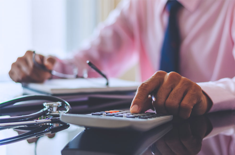 Closeup of physicians hands on calculator with stethoscope on desk representing NDBT physician loans