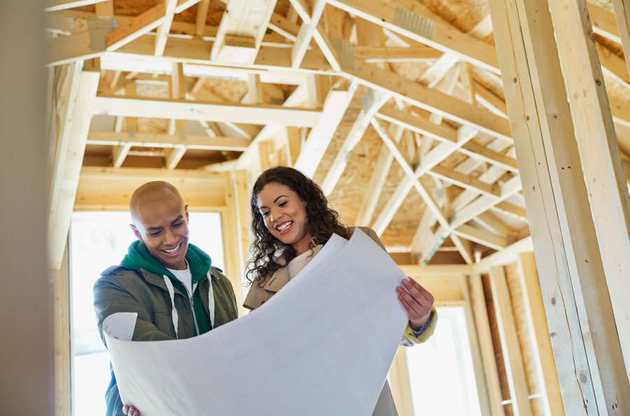 Man and woman looking at blueprint under framing of house.